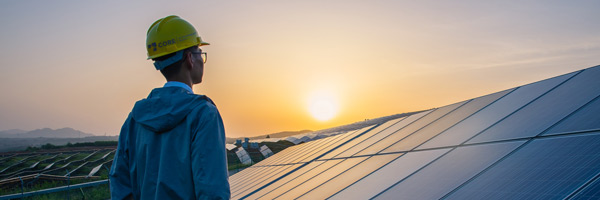 Solar engineer standing in front of a solar panel with a sunset in the background.